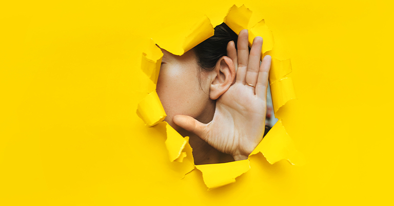 ActiveListen_1 • Roche Leadership A person listening through a hole in yellow paper, hand cupped to ear, symbolizing curiosity and active listening.