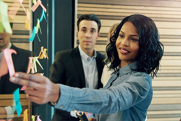 Roche Leadership: Confident businesswoman leading a strategy session, placing sticky notes on a glass wall while team members observe.